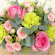Arrangement floral Agatha rond avec roses roses, œillets verts et feuillage dans une corbeille