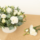 Arrangement floral Nacre avec lisianthus blancs, œillets blancs et eucalyptus dans contenant blanc