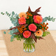 Bouquet d'automne aux tons orange, corail et cuivré avec feuillage gris vert dans un vase en verre