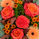 Bouquet d'automne aux tons orange, corail et cuivré avec feuillage gris vert dans un vase en verre