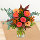 Bouquet d'automne aux tons orange, corail et cuivré avec feuillage gris vert dans un vase en verre