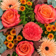 Bouquet d'automne aux tons orange, corail et cuivré avec feuillage gris vert dans un vase en verre