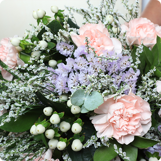 Photo du Bouquet Bienvenue – bouquet rond aux œillets roses, statice lavande, limonium et feuillage vert élégant dans un vase.