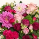 Bouquet de saison rond aux tons roses et fuchsia avec feuillage vert dans un vase en verre