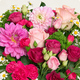 Bouquet de saison rond aux tons roses et fuchsia avec feuillage vert dans un vase en verre