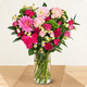 Bouquet de saison rond aux tons roses et fuchsia avec feuillage vert dans un vase en verre