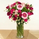 Bouquet Octobre Rose rond aux tons roses et fuchsia avec petites fleurs blanches dans un vase en verre