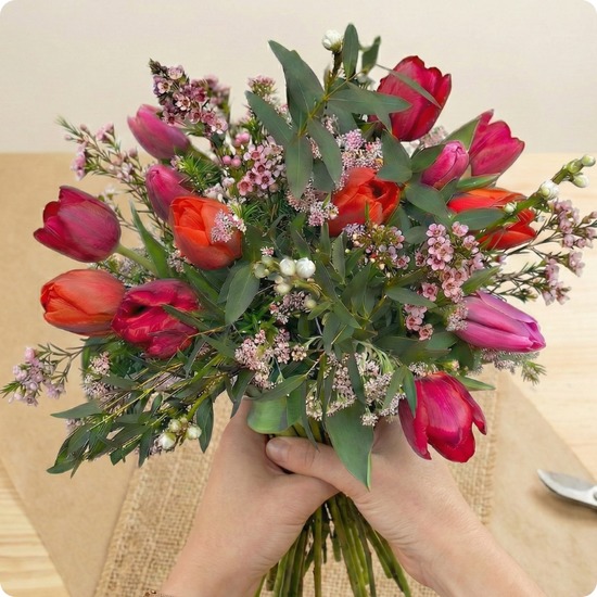 Bouquet rond de tulipes rouges, fuchsia et corail avec feuillage et fleurs de cire