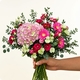 Bouquet Panache avec hortensia rose, lisianthus cerise, gerberas fuchsia et eucalyptus dans un vase en verre