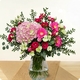 Bouquet Panache avec hortensia rose, lisianthus cerise, gerberas fuchsia et eucalyptus dans un vase en verre